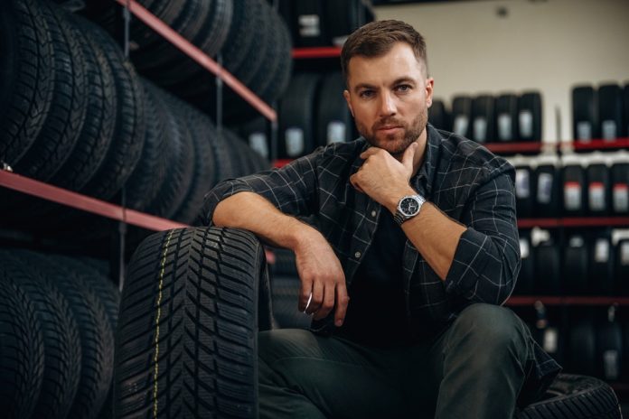 Thinking, sitting. Man worker is maintenance station with tires, wheels